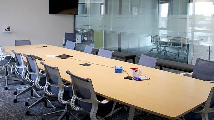 Conference room with large table, 12 chairs, overhead monitor, and glass wall