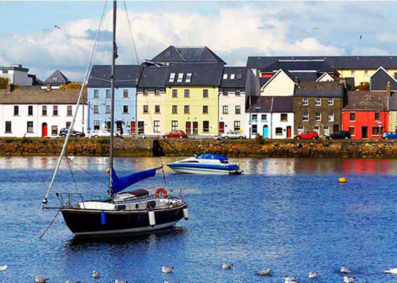 The Claddagh in Galway. Boats are moored in the foreground, and colorful buildings overlook the water.